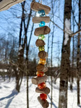 Decorative hanging mobile with colorful beads and wooden sticks against a snowy forest background